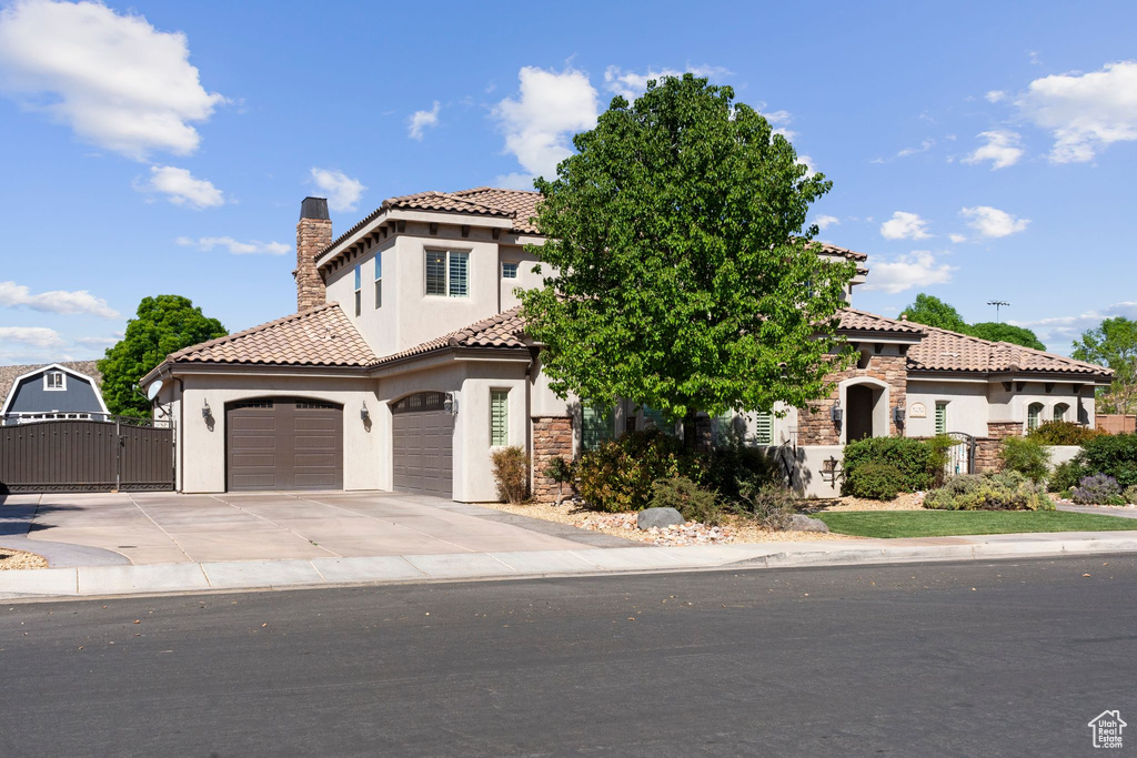 Mediterranean / spanish-style home with concrete driveway, a chimney, an attached garage, a tile roof, and a gate