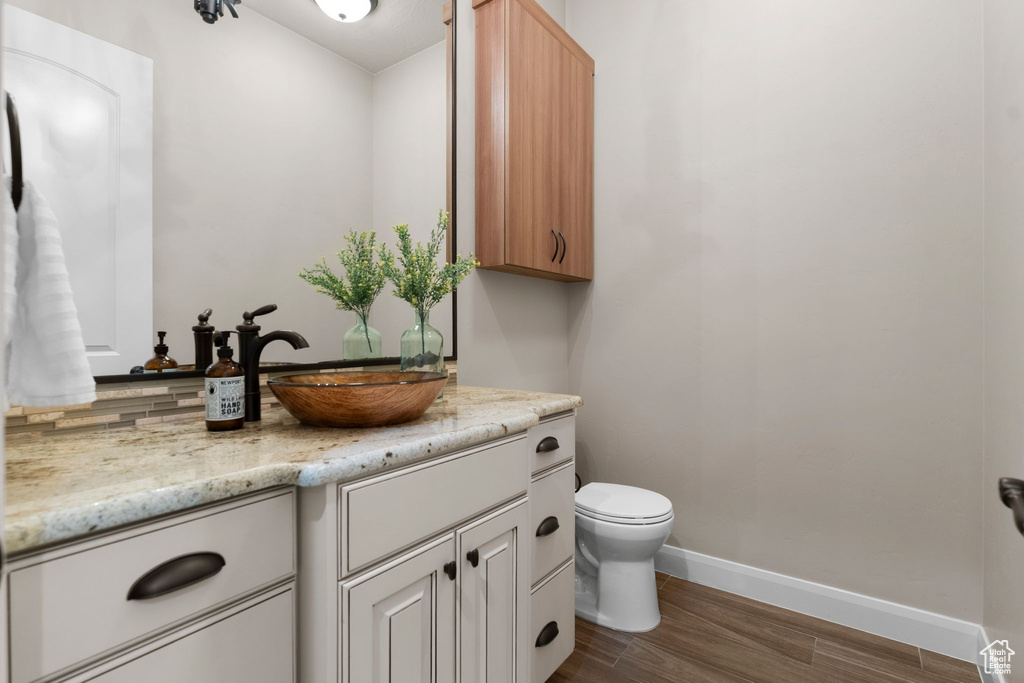 Half bathroom featuring vanity, baseboards, toilet, and wood finished floors