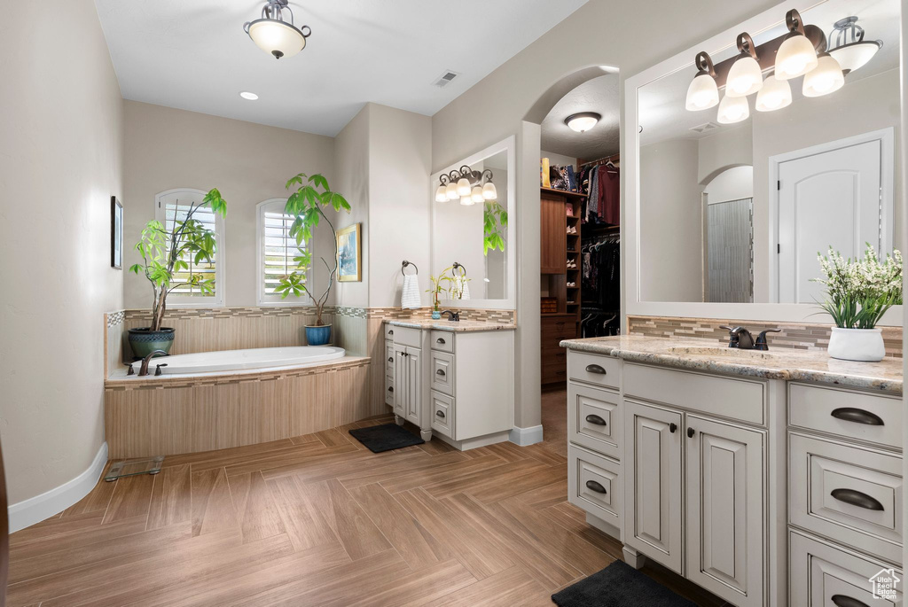 Bathroom with two vanities, a garden tub, visible vents, a sink, and baseboards