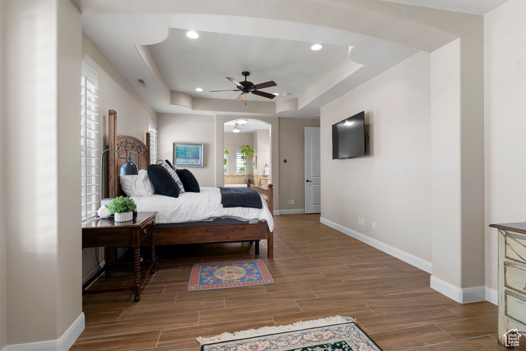 Bedroom with arched walkways, a tray ceiling, baseboards, and wood finished floors