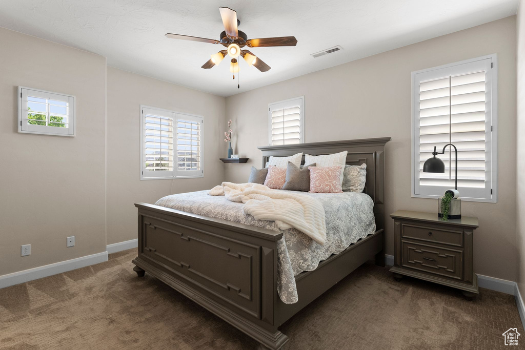 Carpeted bedroom featuring visible vents, multiple windows, baseboards, and ceiling fan