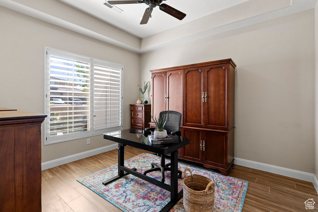 Home office with light wood-style floors, baseboards, visible vents, and ceiling fan