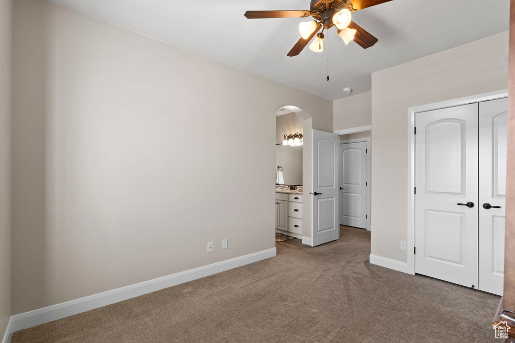 Unfurnished bedroom with a closet, baseboards, arched walkways, a ceiling fan, and light carpet