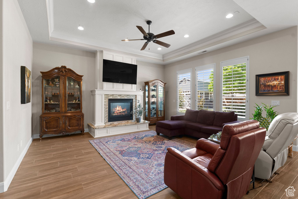 Living room with baseboards, a fireplace, a ceiling fan, a raised ceiling, and light wood finished floors
