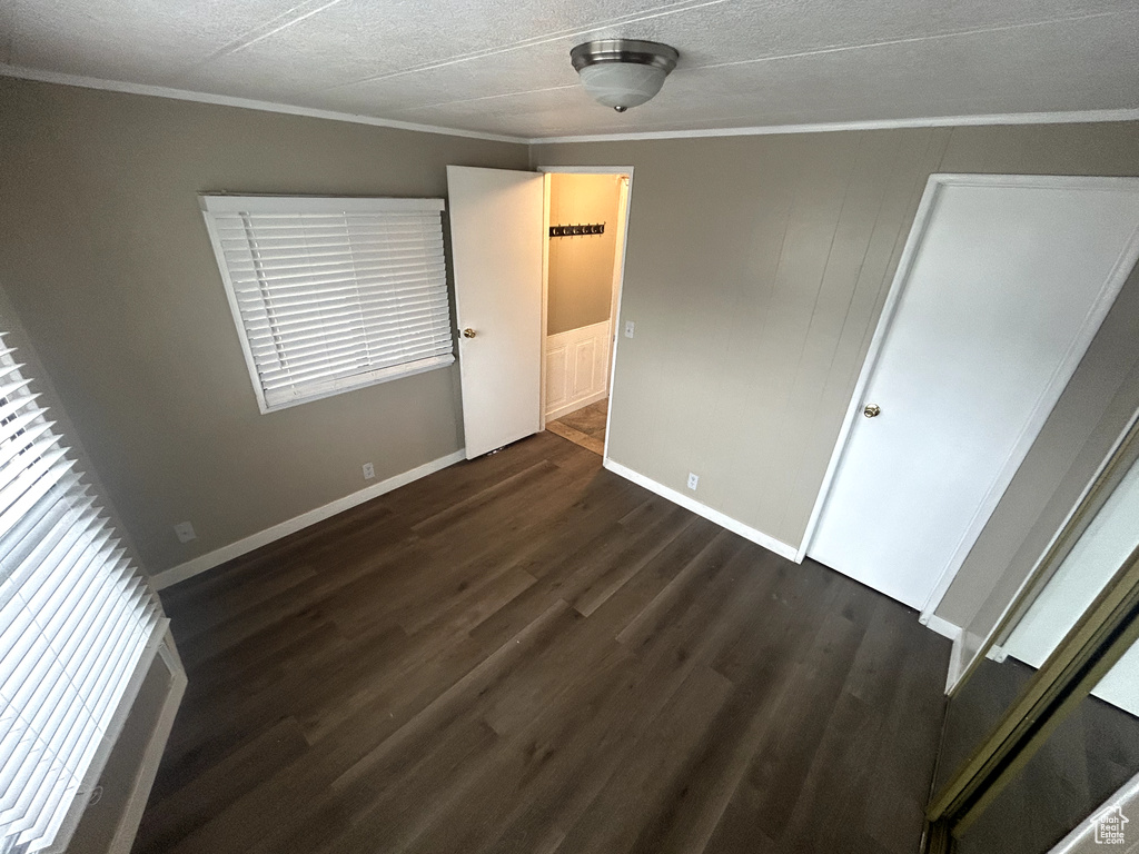 Unfurnished bedroom with dark wood-type flooring, baseboards, ornamental molding, and a textured ceiling