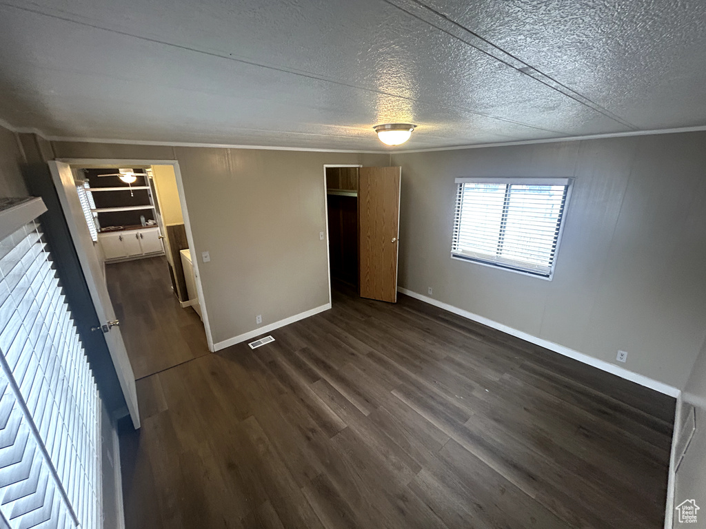Unfurnished bedroom with crown molding, visible vents, baseboards, and dark wood-type flooring