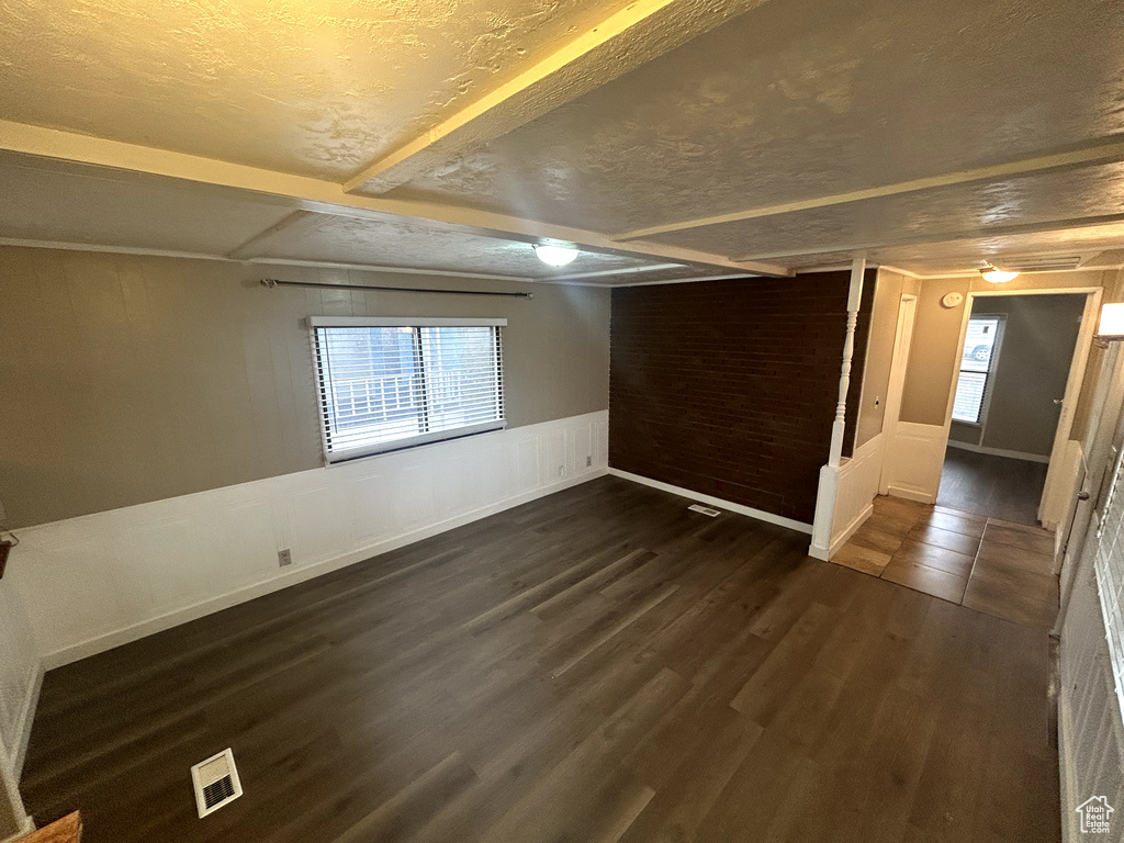 Basement featuring dark wood-style flooring, a textured ceiling, visible vents, and wainscoting