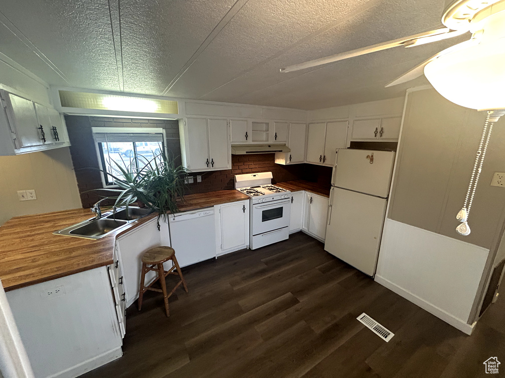 Kitchen with white appliances, a textured ceiling, visible vents, a sink, and wood counters