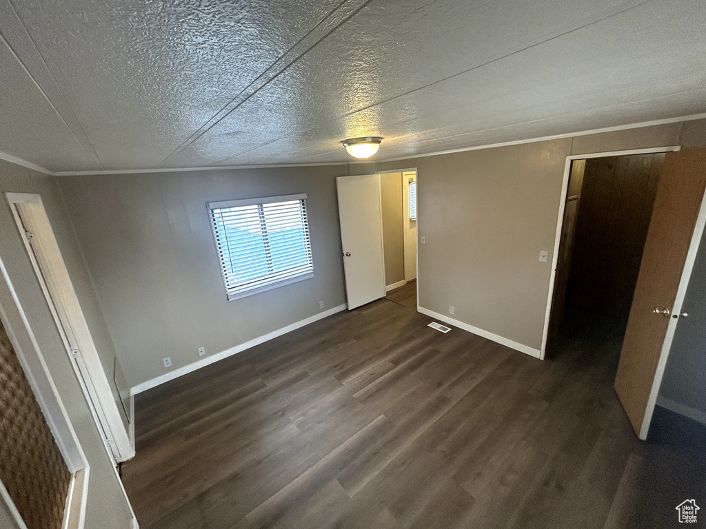 Unfurnished bedroom featuring visible vents, baseboards, a textured ceiling, crown molding, and dark wood-type flooring