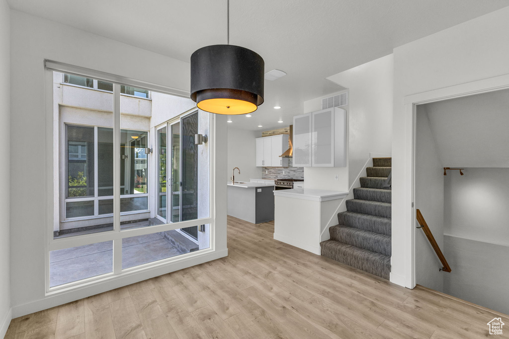 Kitchen with light countertops, light wood finished floors, high end stove, white cabinetry, and backsplash