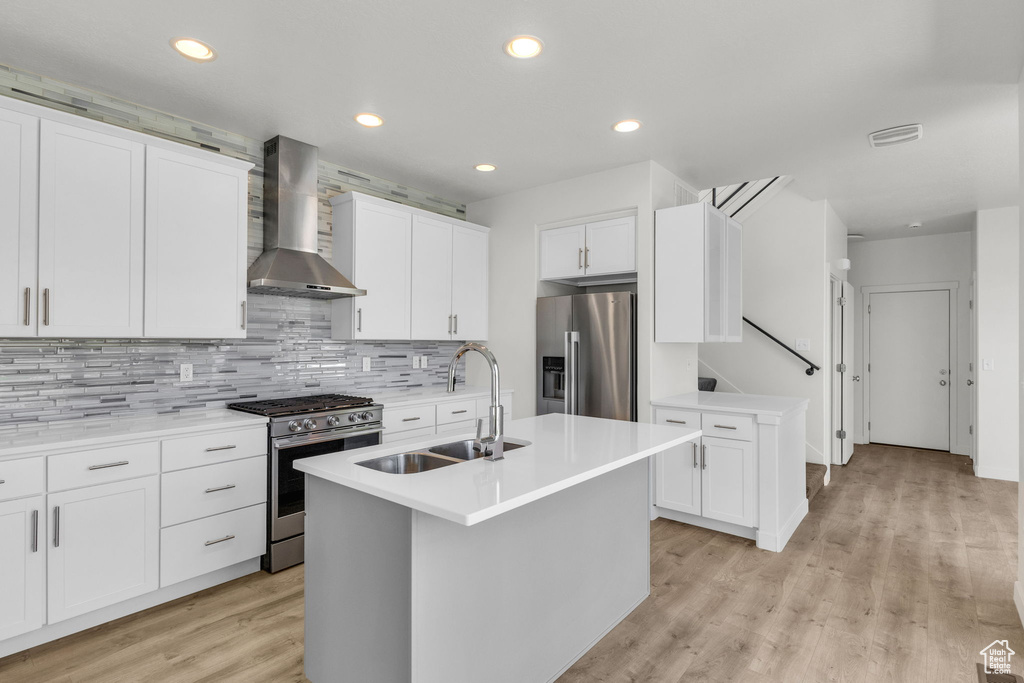 Kitchen featuring stainless steel appliances, a sink, wall chimney exhaust hood, backsplash, and light countertops