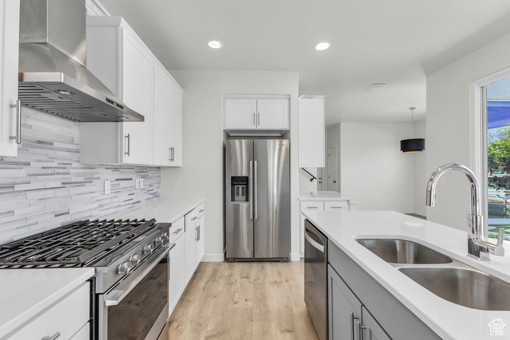 Kitchen featuring appliances with stainless steel finishes, wall chimney range hood, a sink, backsplash, and light wood finished floors