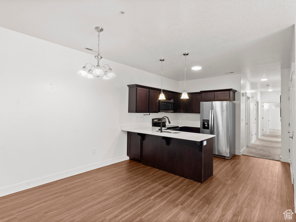 Kitchen featuring a peninsula, dark brown cabinets, a breakfast bar area, appliances with stainless steel finishes, and a sink