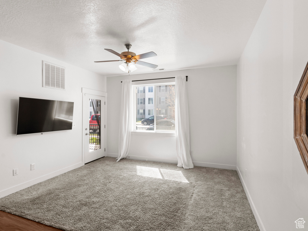 Unfurnished living room featuring baseboards, a textured ceiling, a ceiling fan, carpet floors, and visible vents