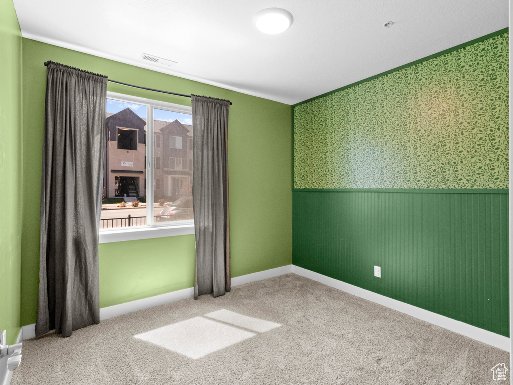 Carpeted empty room with visible vents, baseboards, wainscoting, and wallpapered walls
