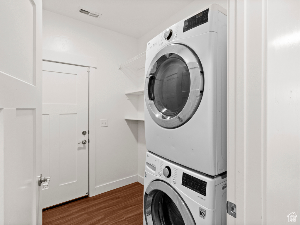 Laundry room with laundry area, dark wood finished floors, stacked washer and dryer, visible vents, and baseboards