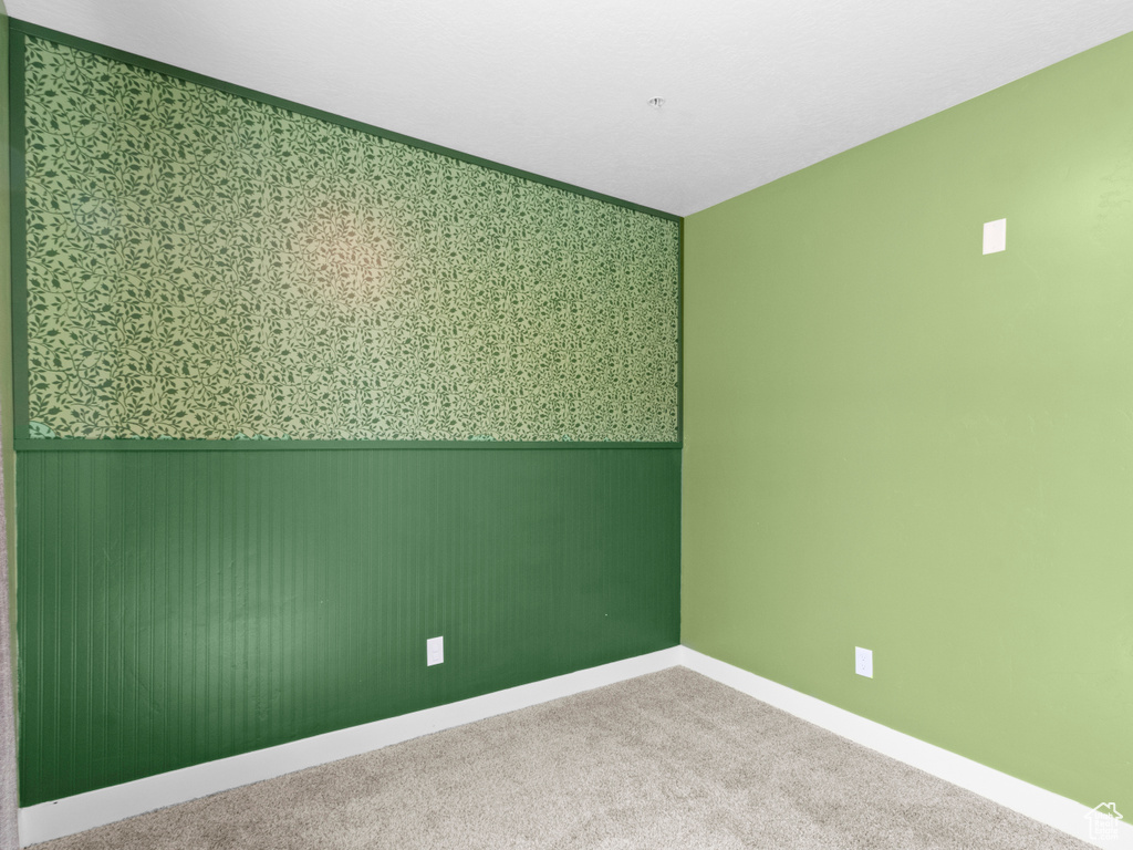 Carpeted empty room with a wainscoted wall, baseboards, and wallpapered walls