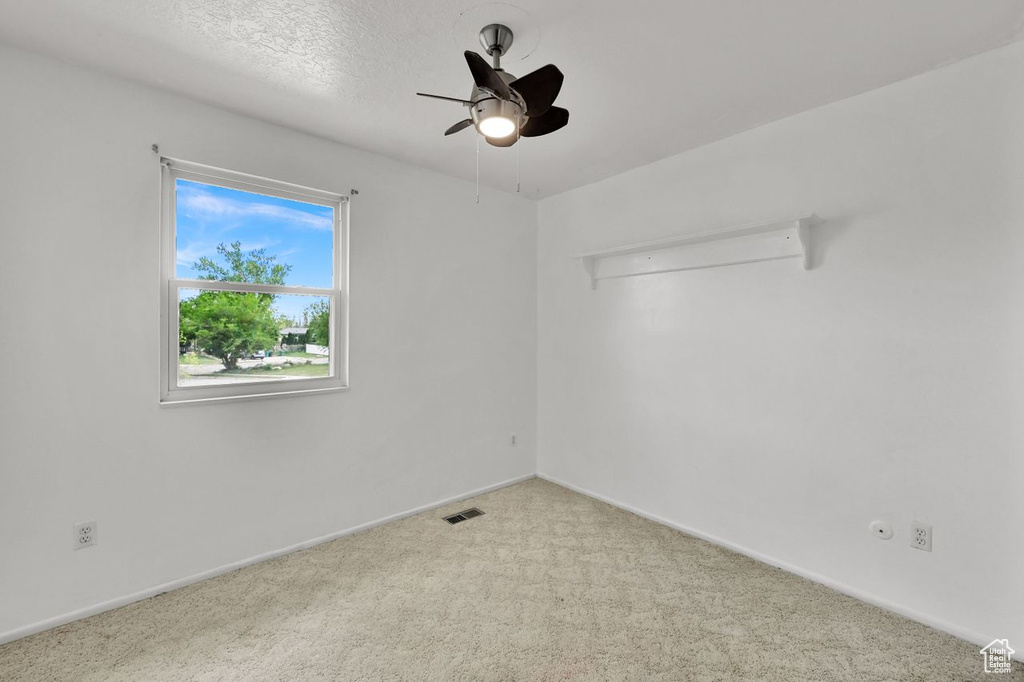 Carpeted empty room featuring ceiling fan, baseboards, and attic access