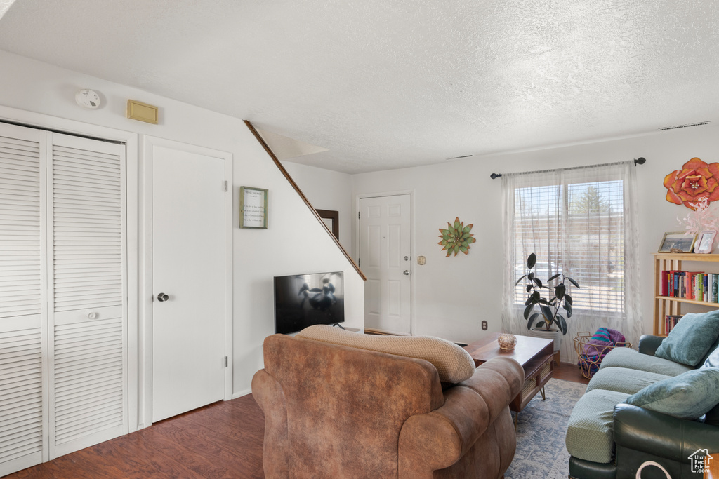 Living room with a textured ceiling, dark wood-style floors, and stairway