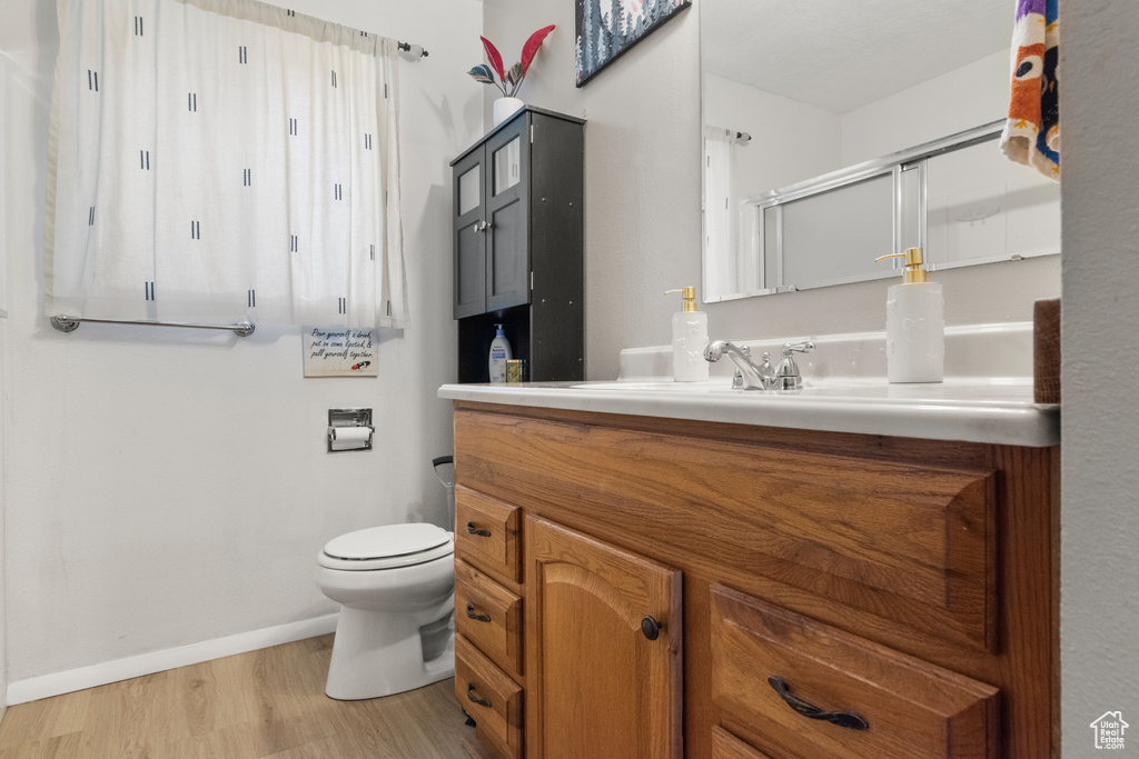 Full bathroom with a shower with shower door, vanity, toilet, wood finished floors, and baseboards