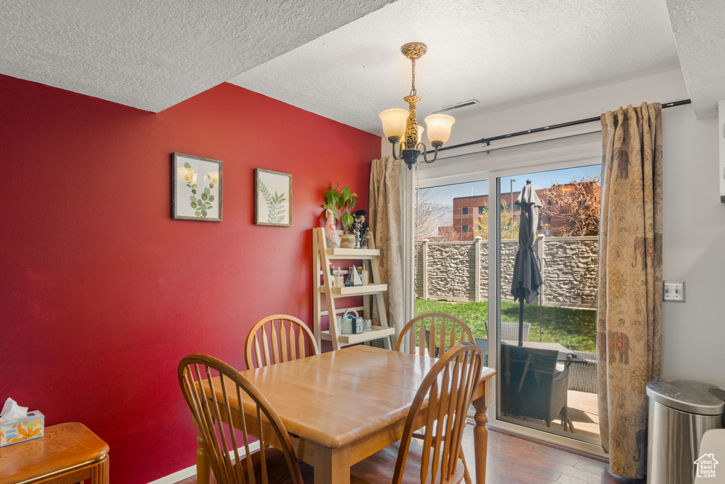 Dining space with visible vents, a textured ceiling, an inviting chandelier, and wood finished floors