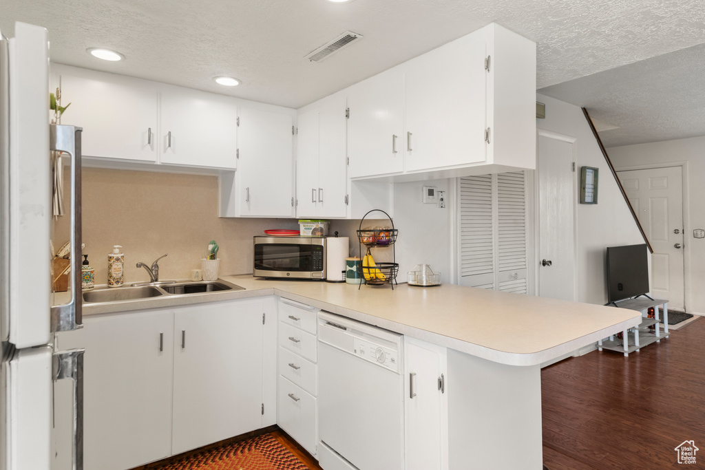 Kitchen featuring stainless steel microwave, a peninsula, light countertops, white dishwasher, and a sink