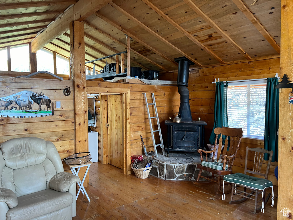 Living area featuring a wood stove, lofted ceiling with beams, wooden ceiling, wood walls, and hardwood / wood-style flooring