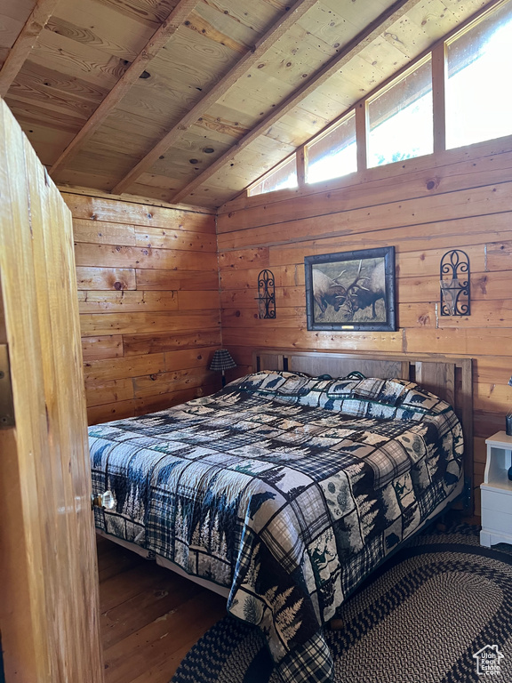 Bedroom with wooden walls, hardwood / wood-style flooring, vaulted ceiling with beams, and wood ceiling