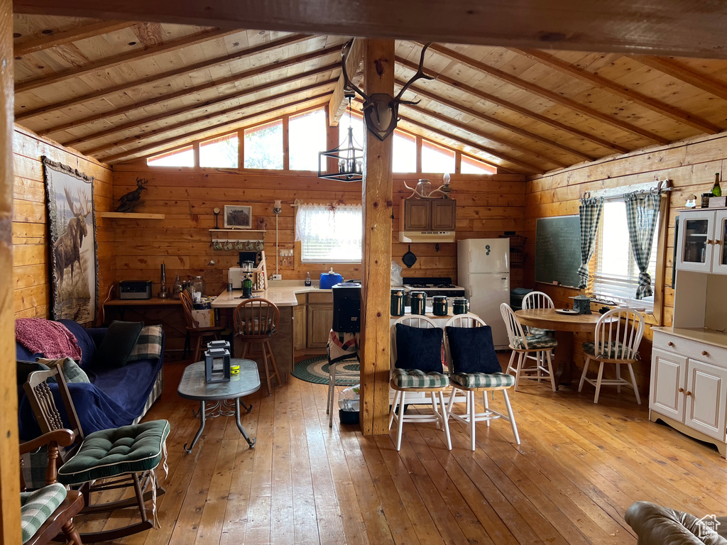 Living room with wood walls, wooden ceiling, light wood finished floors, and vaulted ceiling with beams