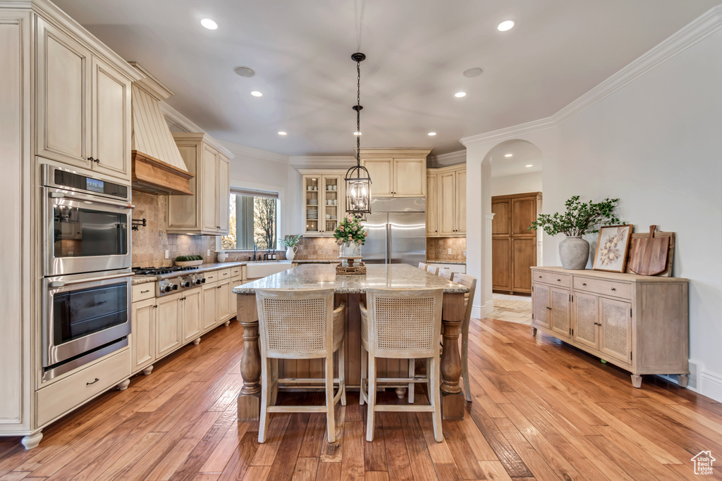 Kitchen with appliances with stainless steel finishes, crown molding, cream cabinetry, decorative backsplash, and light stone counters