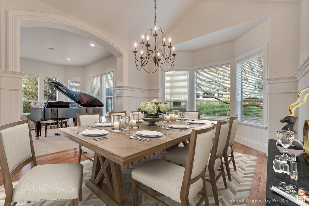 Dining area with a notable chandelier, light wood-style flooring, wainscoting, a decorative wall, and arched walkways