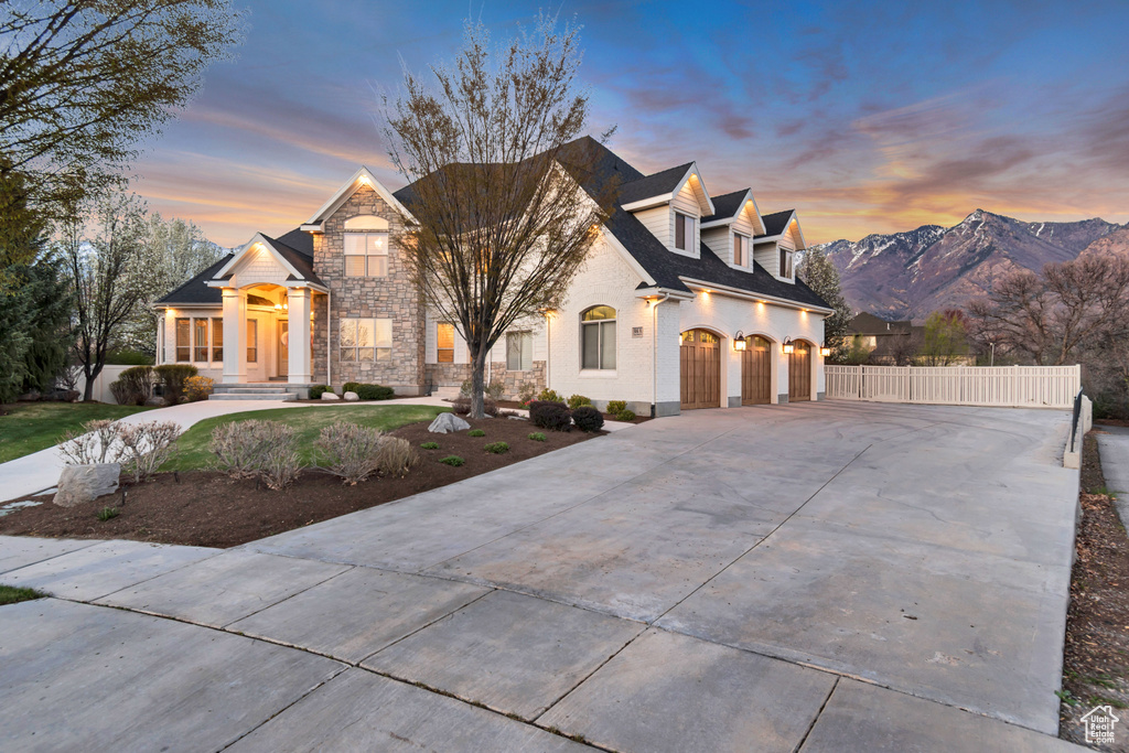 View of front of home featuring a mountain view, stone siding, a garage, fence, and concrete driveway