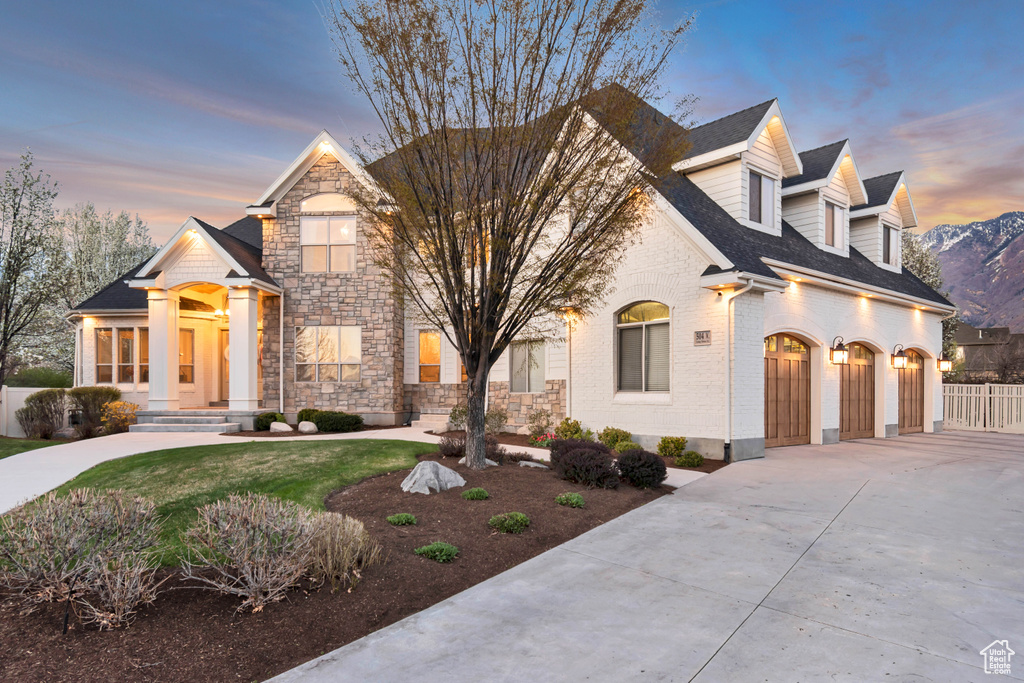 View of front of house featuring roof with shingles, driveway, stone siding, and fence