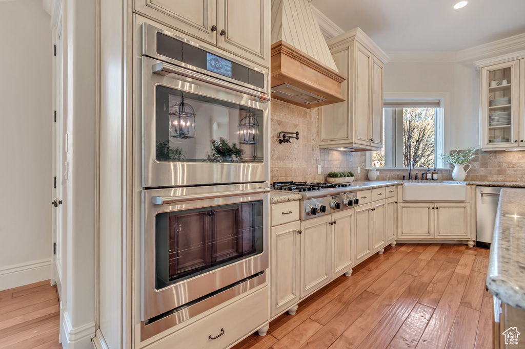 Kitchen featuring custom range hood, cream cabinets, light wood-style floors, stainless steel appliances, and a sink
