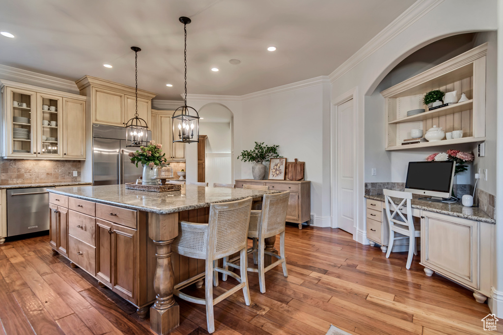 Kitchen featuring light wood-type flooring, built in study area, a center island, backsplash, and appliances with stainless steel finishes