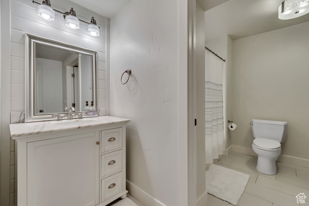Full bath featuring a shower with shower curtain, vanity, baseboards, and toilet