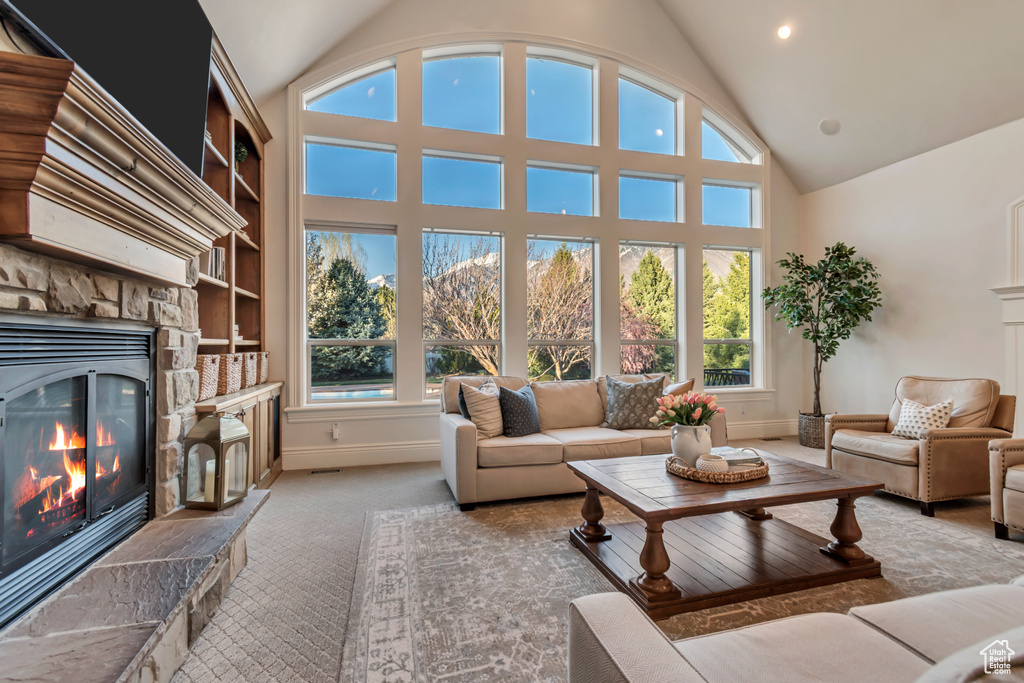 Carpeted living area with high vaulted ceiling, baseboards, a stone fireplace, and recessed lighting