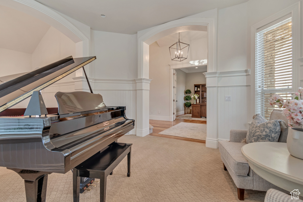 Living area featuring a chandelier, arched walkways, light colored carpet, and a wainscoted wall