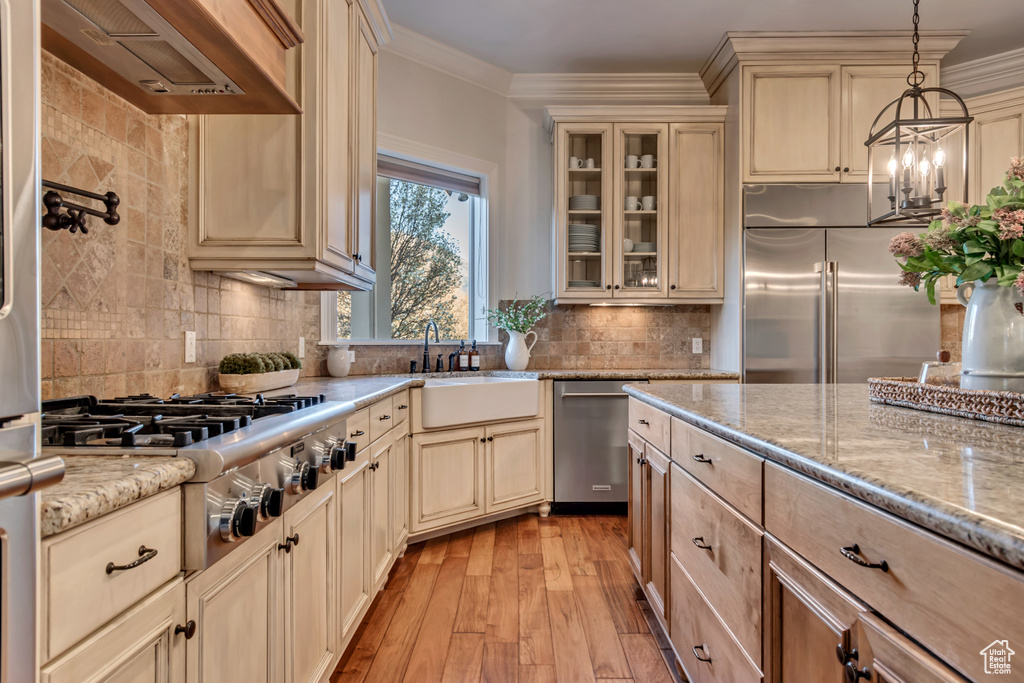 Kitchen featuring wall chimney range hood, cream cabinets, a sink, stainless steel appliances, and light wood finished floors