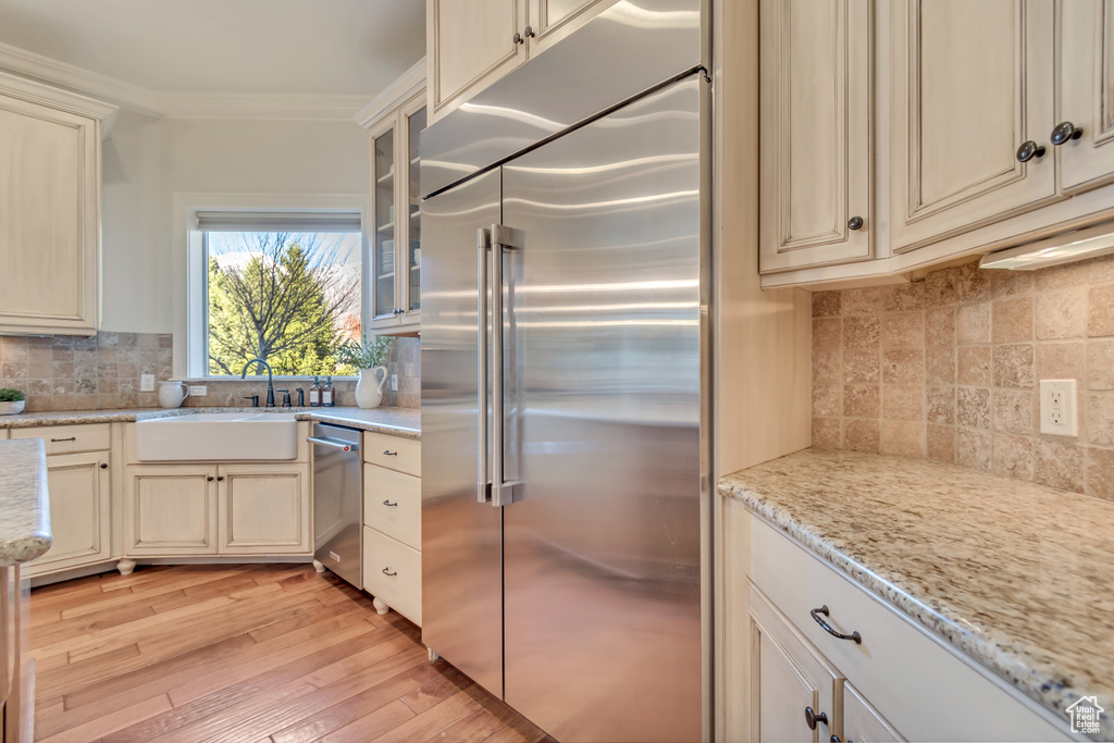 Kitchen with light wood-style flooring, crown molding, cream cabinetry, stainless steel appliances, and a sink