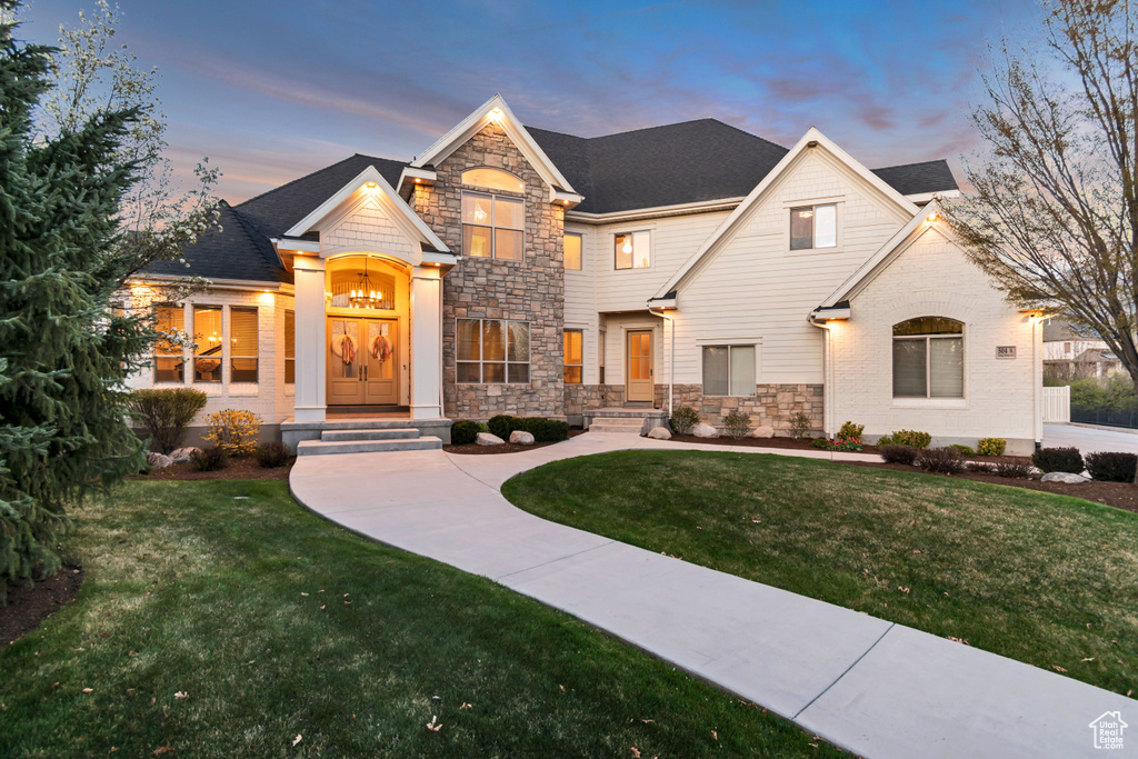 View of front of house with a yard, a shingled roof, and stone siding