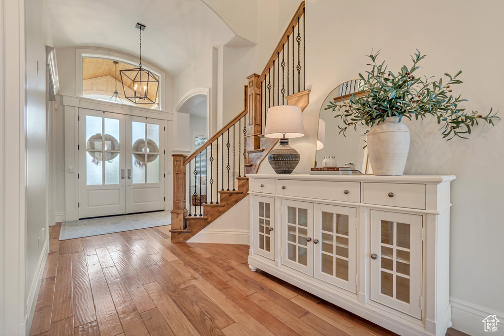 Foyer entrance featuring french doors, light wood finished floors, an inviting chandelier, and stairs
