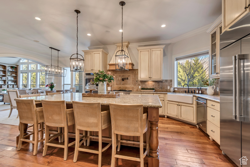 Kitchen with custom exhaust hood, crown molding, cream cabinetry, stainless steel appliances, and a sink