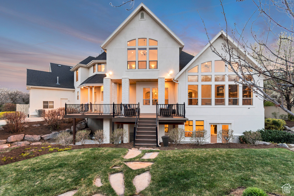 Back of property at dusk with a deck, a yard, stairs, stucco siding, and roof with shingles