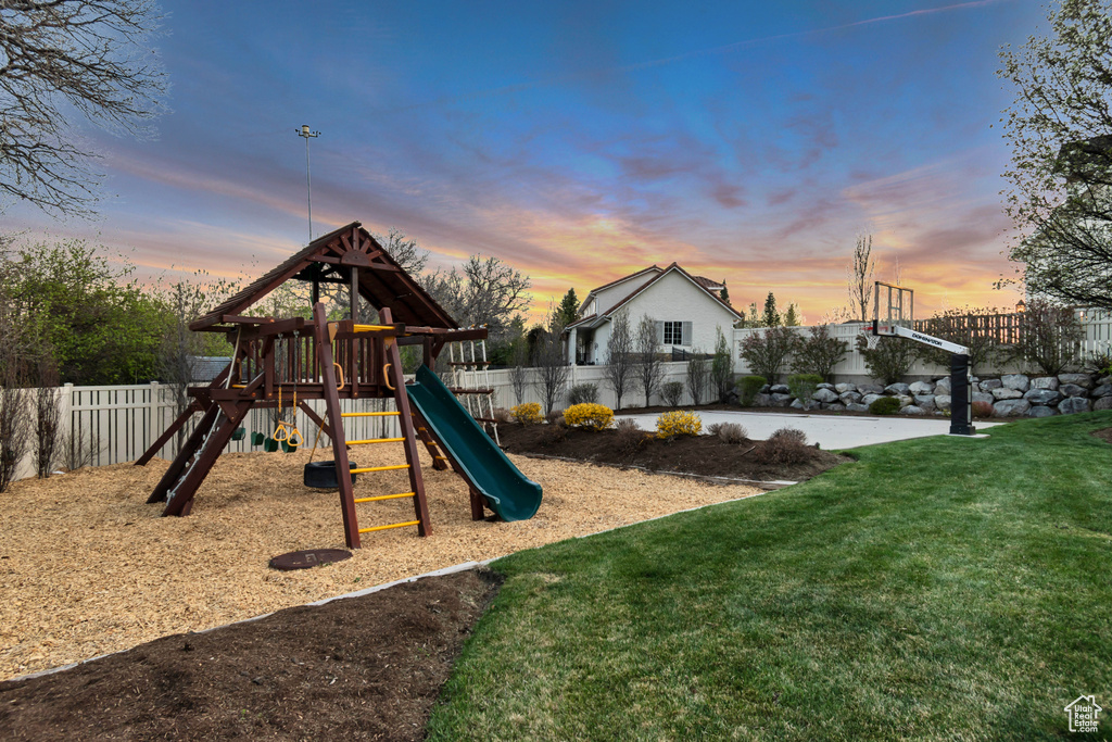 Playground at dusk featuring fence, a lawn, and a playground