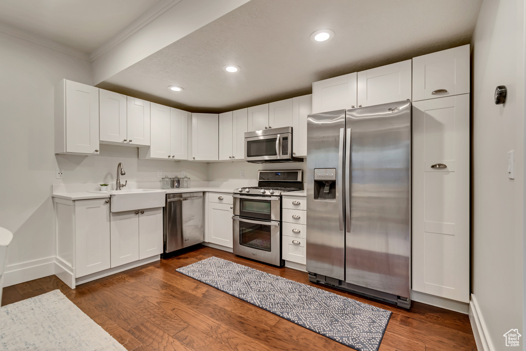 Kitchen with ornamental molding, white cabinets, appliances with stainless steel finishes, a sink, and light countertops