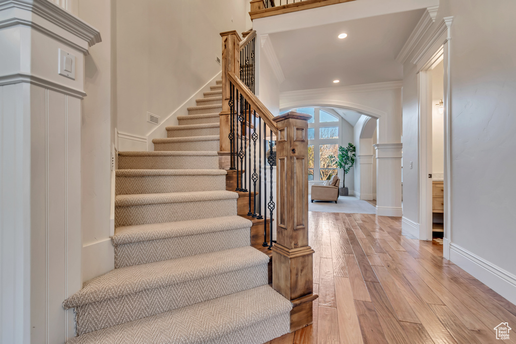 Staircase with arched walkways, ornate columns, ornamental molding, recessed lighting, and wood-type flooring