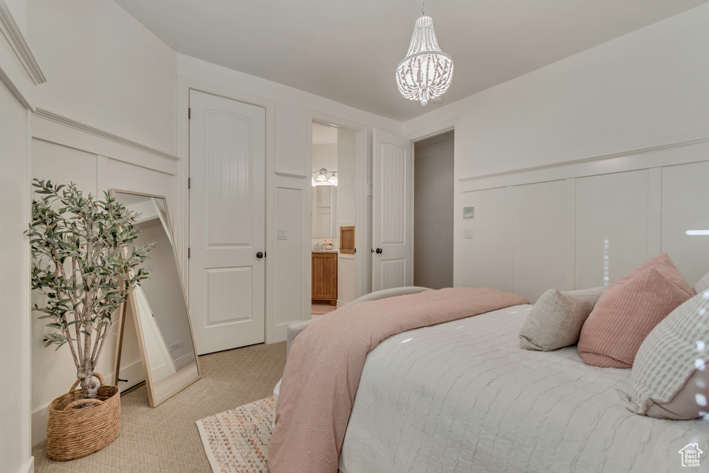 Bedroom with a decorative wall, a wainscoted wall, an inviting chandelier, and light colored carpet