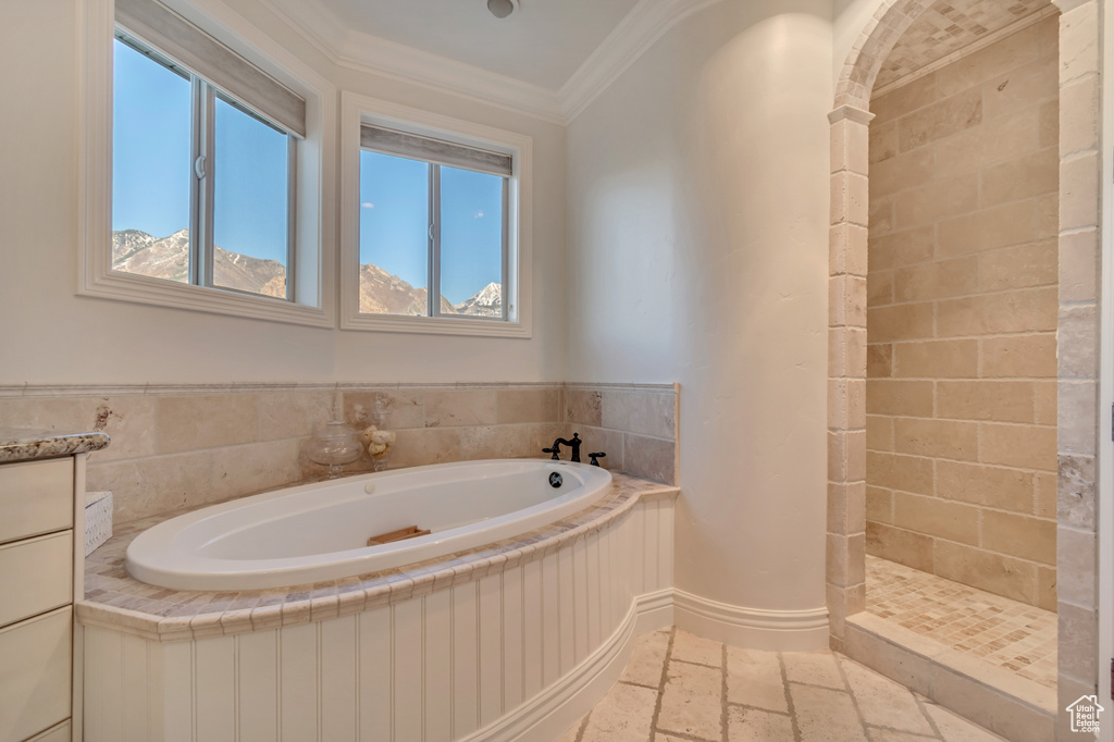 Bathroom with baseboards, crown molding, stone tile flooring, tiled shower, and a garden tub
