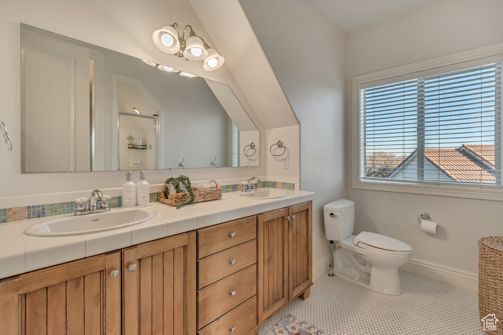 Bathroom with toilet, double vanity, a sink, and walk in shower